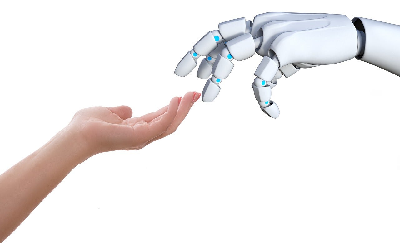 Een robothand en mensenhand die elkaar licht aanraken
