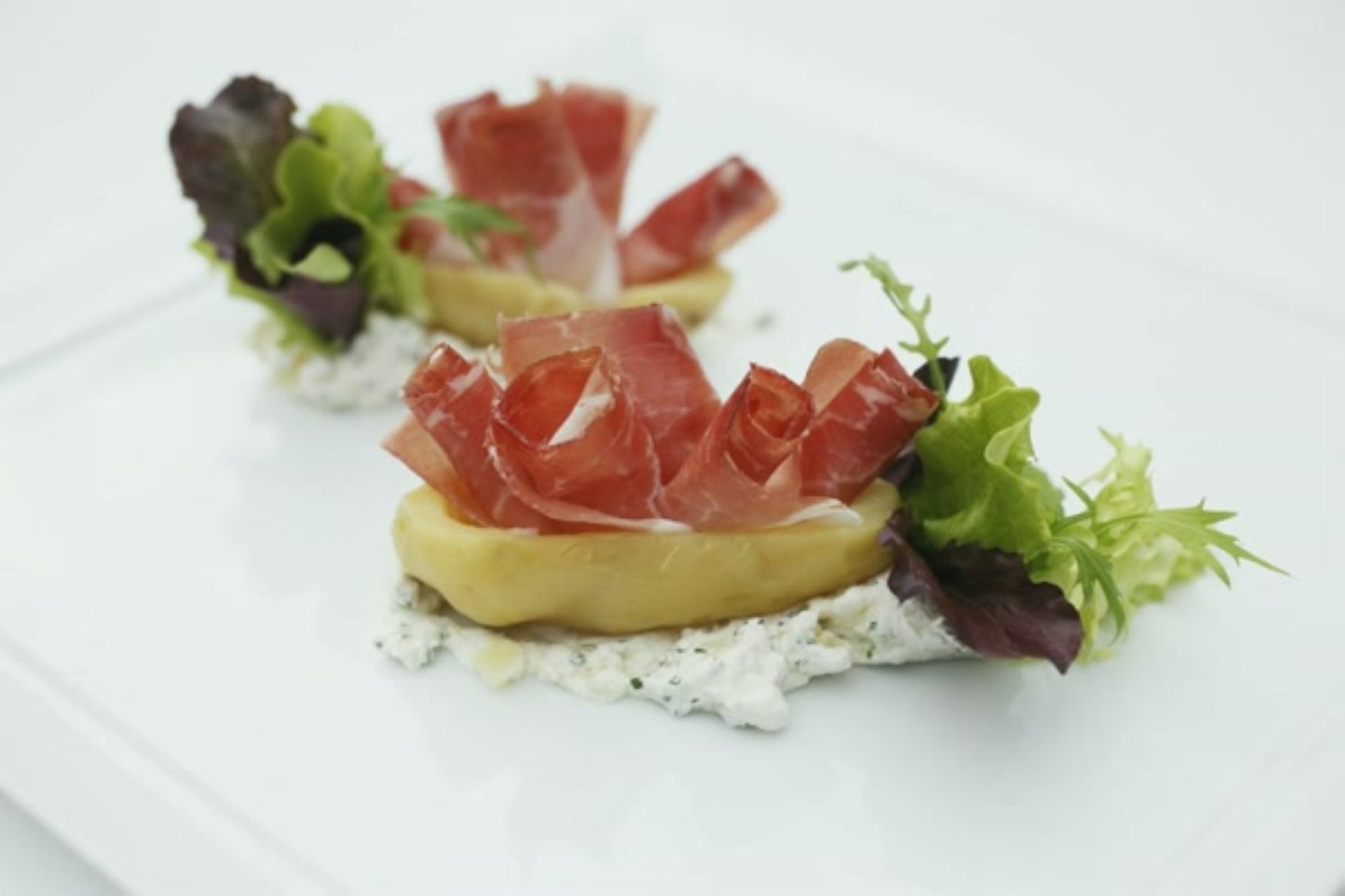 Mit Südtiroler Speck g.g.A. gefüllte Kartoffeln, serviert auf cremigem Frischkäse mit Blattsalat.