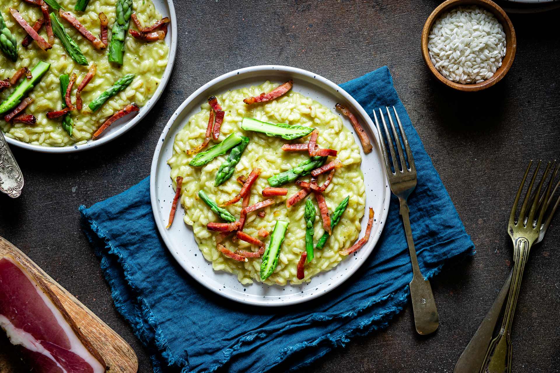 Cremiges grünes Spargelrisotto, garniert mit Südtiroler Speck g.g.A. und Spargelspitzen.