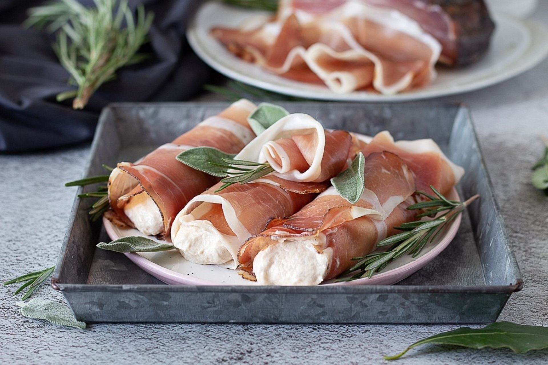 South Tyrolean speck cannoli filled with a creamy filling, served on a plate with aromatic herbs.