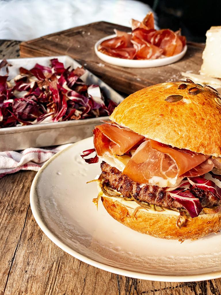 Burger gourmet avec steak haché de bœuf, artichauts, radicchio et Speck du Tyrol du Sud IGP, servi dans un pain doré.