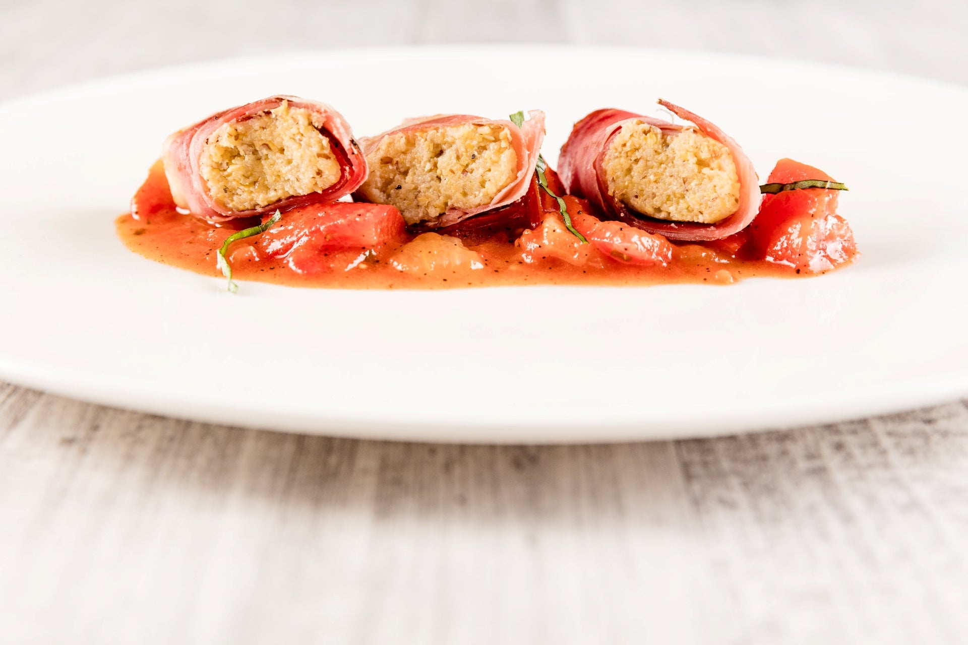 In Speck gewickelte Polenta auf Paprika-Peperonata, elegant angerichtet auf einem weißen Teller.