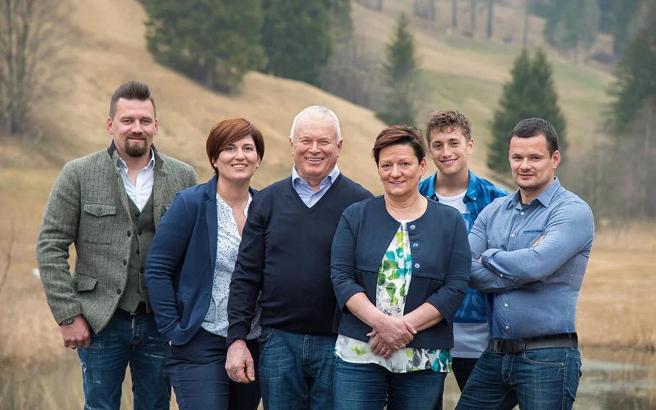 Familie Kofler posiert im Freien auf einer Wiese mit Bäumen im Hintergrund