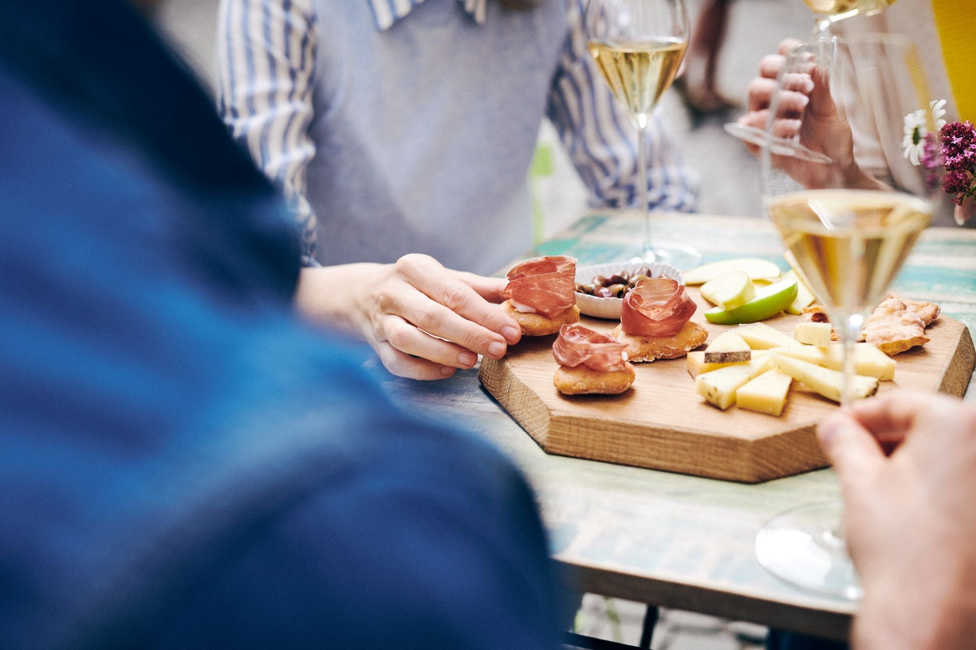 Personen am Tisch genießen Häppchen mit Südtiroler Speck g.g.A., Käse und Weißweingläsern.