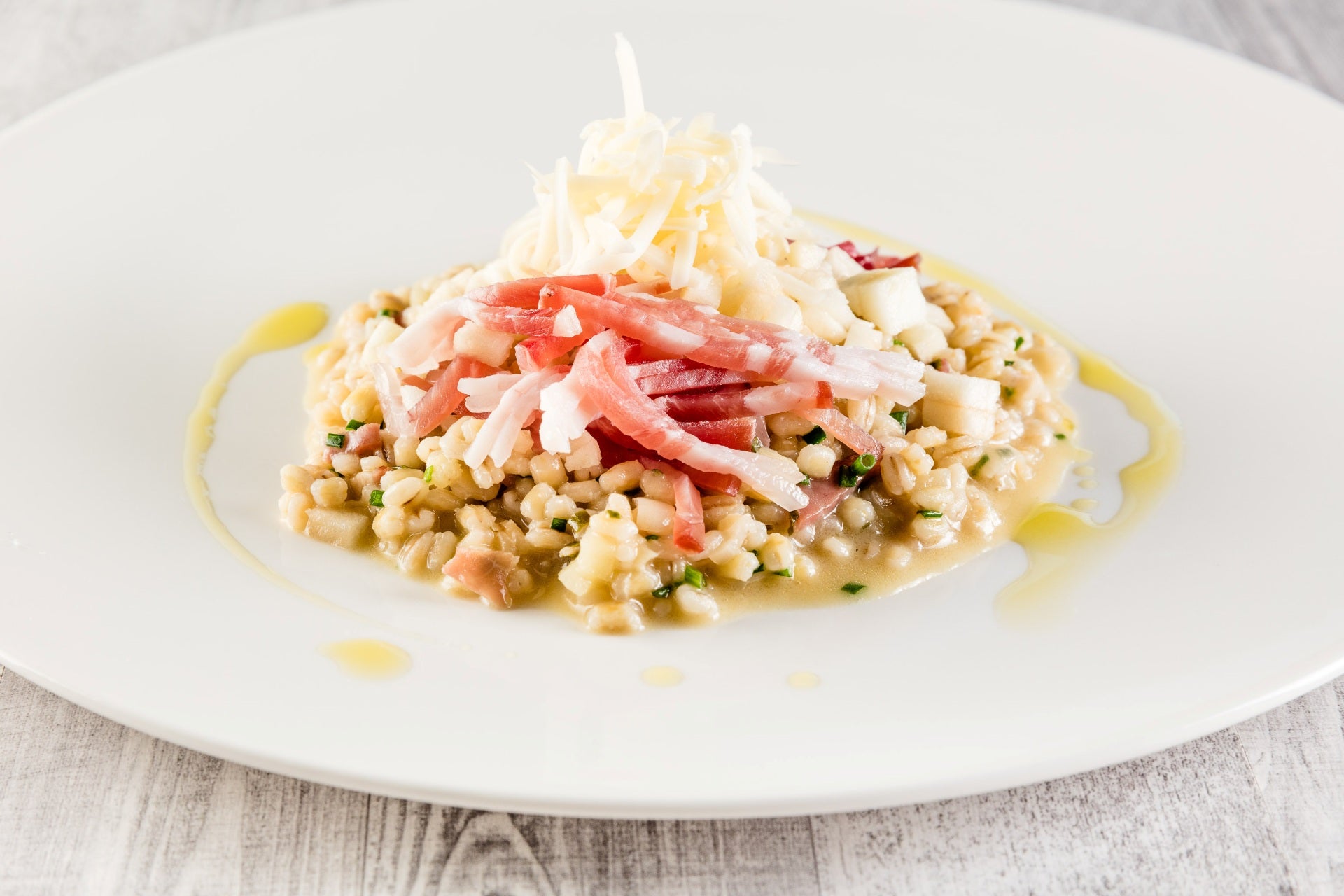 Orzotto mit Speck Alto Adige IGP in Julienne-Streifen geschnitten, Apfeldieben, geriebenem Käse und einem Faden Öl.
