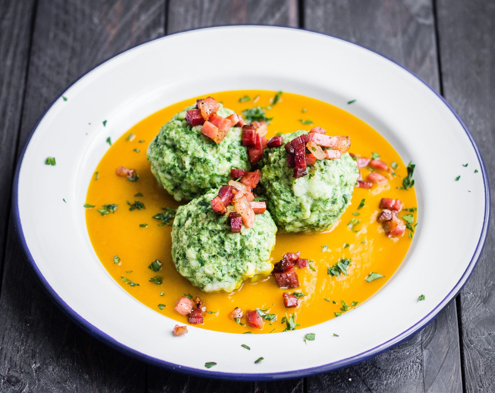 Spinatknödel, serviert auf Kürbiskrem und garniert mit Würfeln von Südtiroler Speck g.g.A.