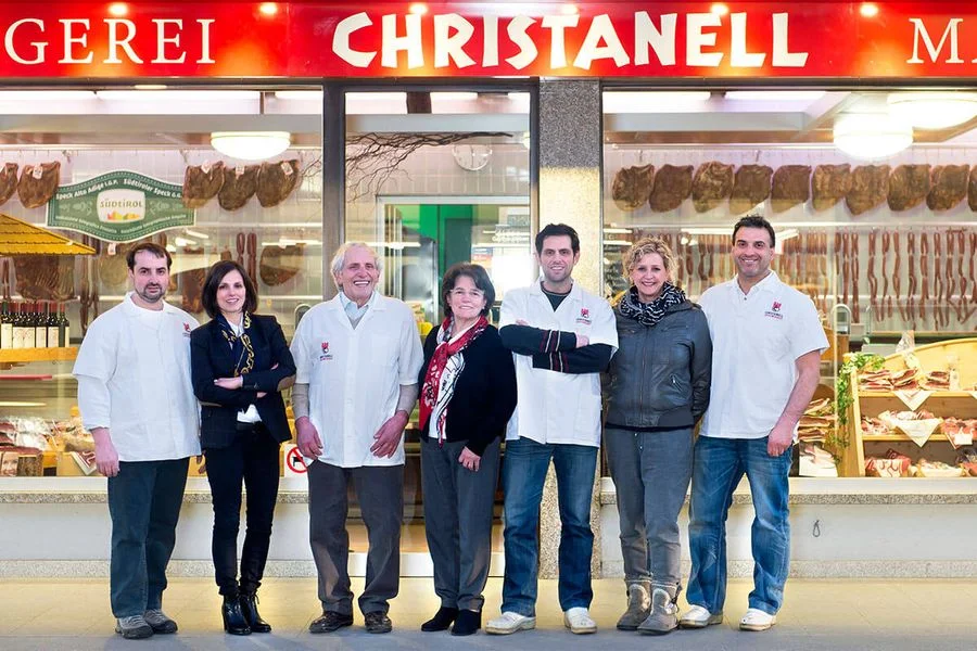 Il team della macelleria Christanell in posa davanti al negozio con insegna sopra l’ingresso
