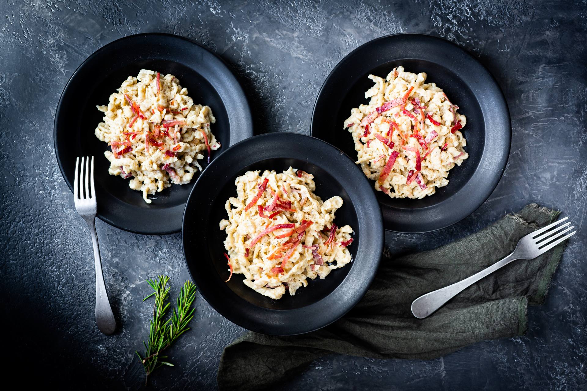 Kremowe spätzle z serem i Speckiem z Południowego Tyrolu ChOG, podane na czarnych talerzach.