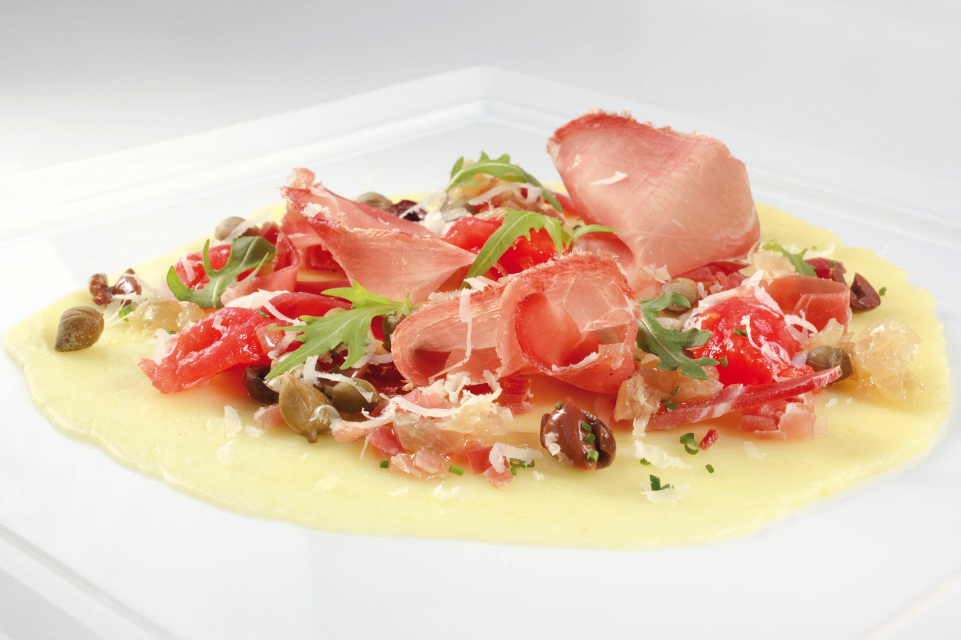 Kartoffelpizza mit Südtiroler Speck, Rucola und gehobeltem Käse, angerichtet auf einem weißen Teller.