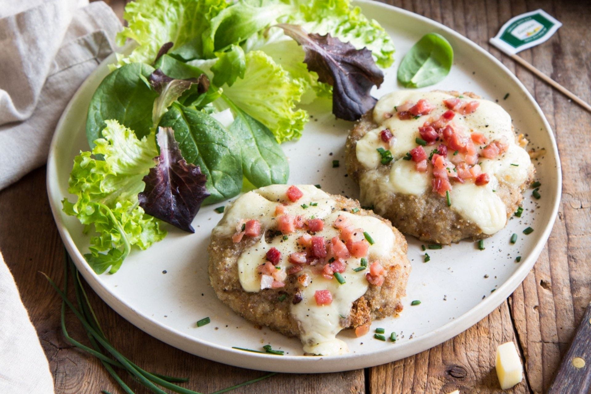 Minced meat mini pizzas topped with South Tyrolean speck and melted cheese, served with fresh salad.