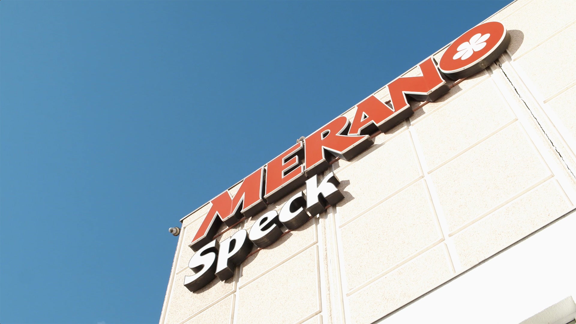 Weiße Fassade des Produktionsstandorts von Merano Speck unter blauem Himmel