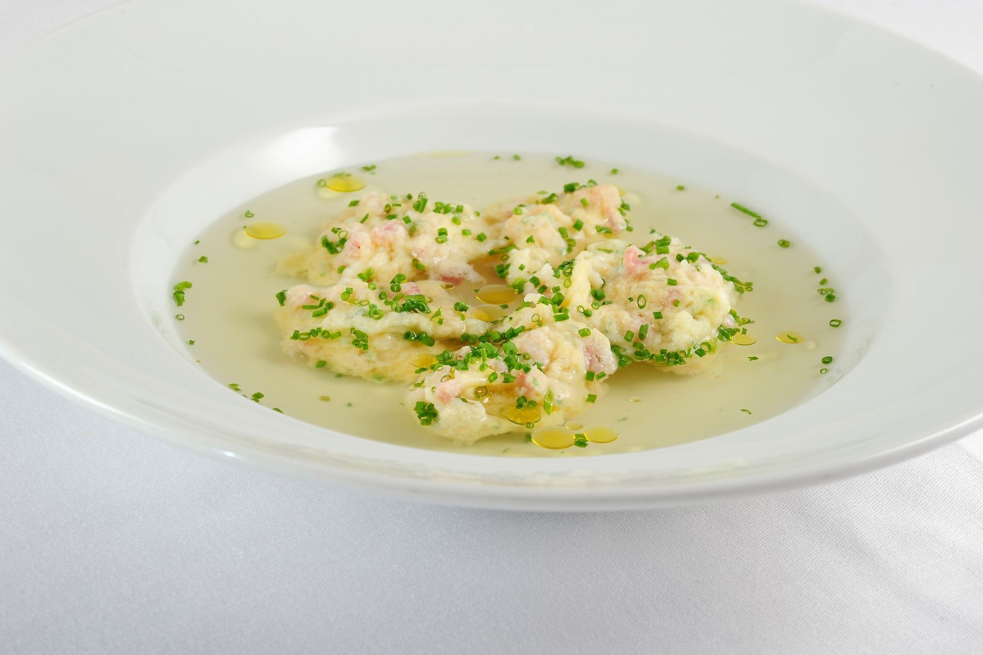 Clear broth with speck dumplings made from South Tyrolean Speck PGI, topped with fresh chives.