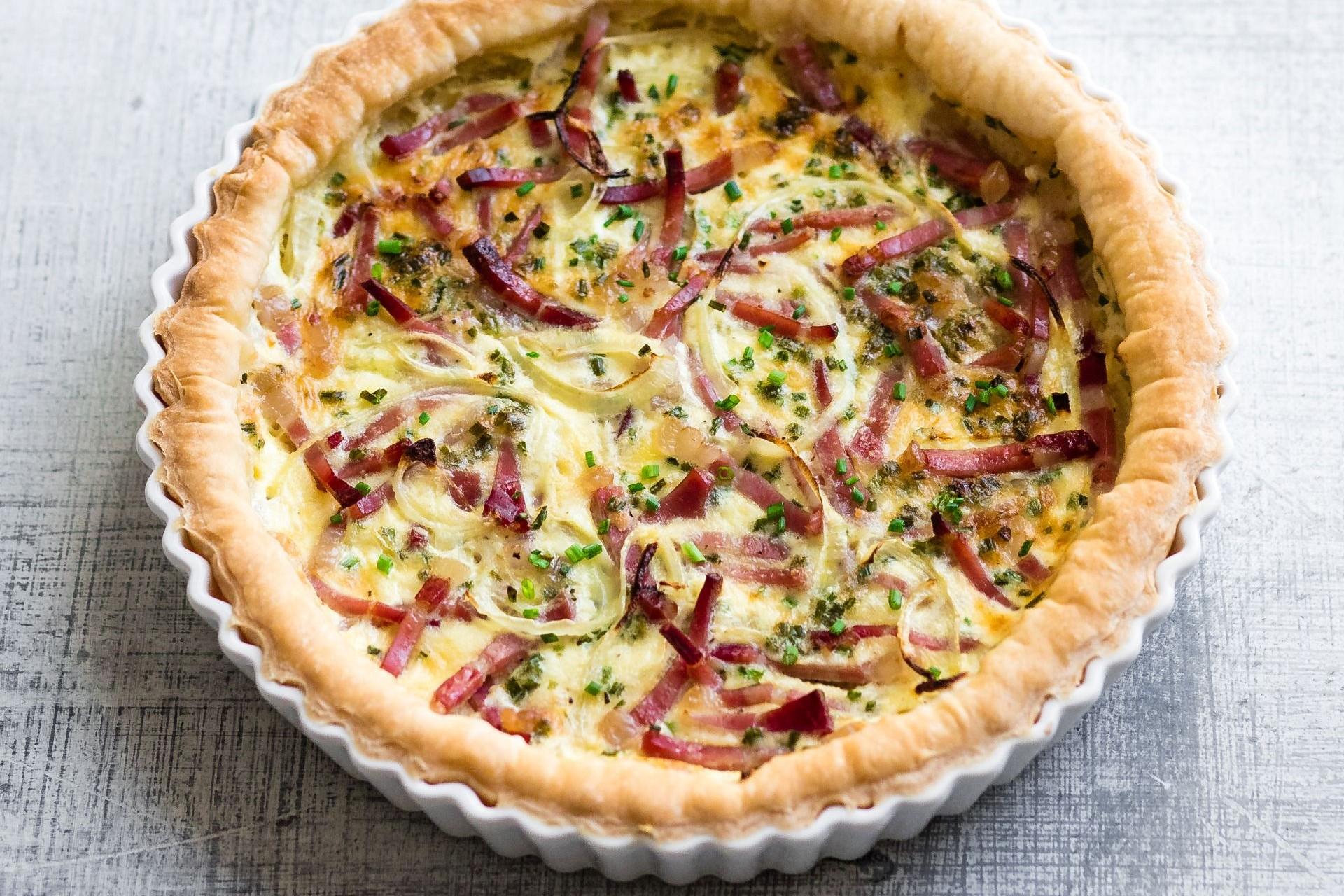 Zwiebelkuchen mit Südtiroler Speck g.g.A., Zwiebeln und Kräutern, gebacken in einer runden Form.