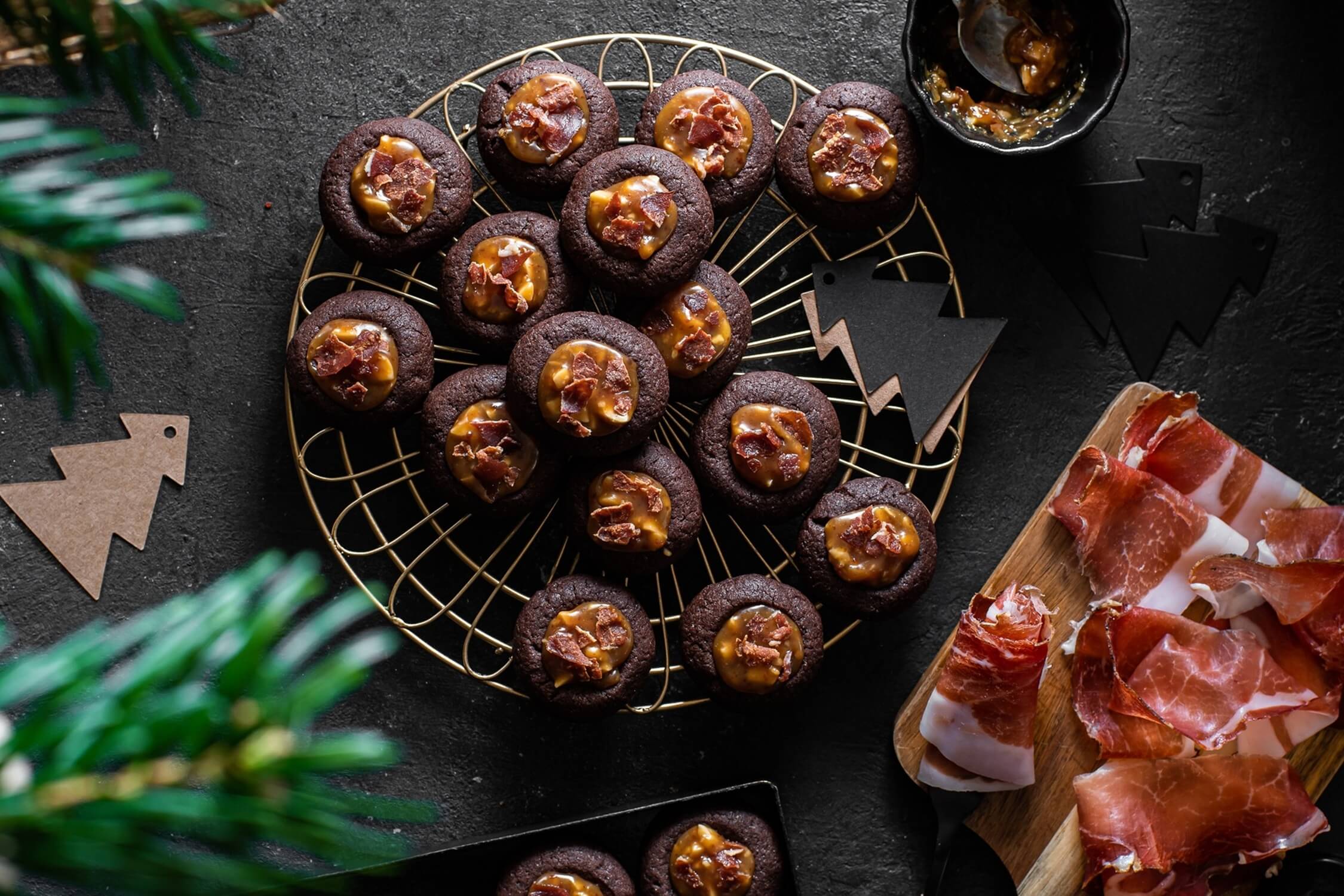 Biscotti al cioccolato con caramello di arachidi e Speck Alto Adige IGP, un mix dolce-salato irresistibile per ogni occasione, disposti su una griglia decorativa con dettagli natalizi.