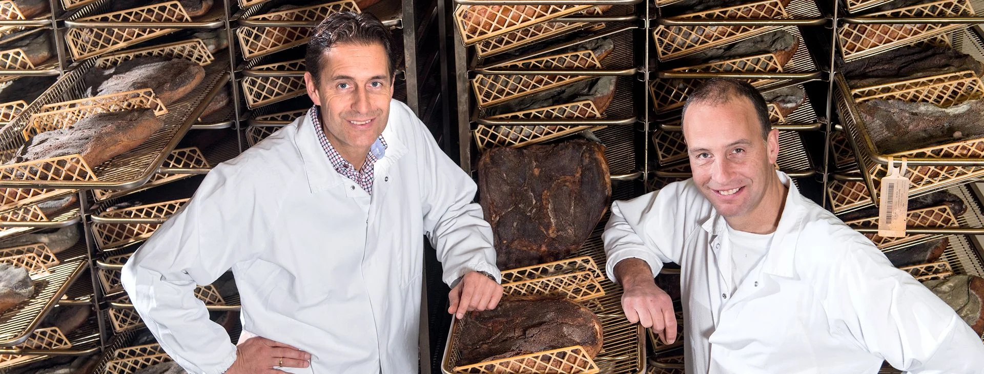 Hersteller der Galloni im Reiferaum vor Regalen mit Südtiroler Speck g.g.A. blicken in die Kamera