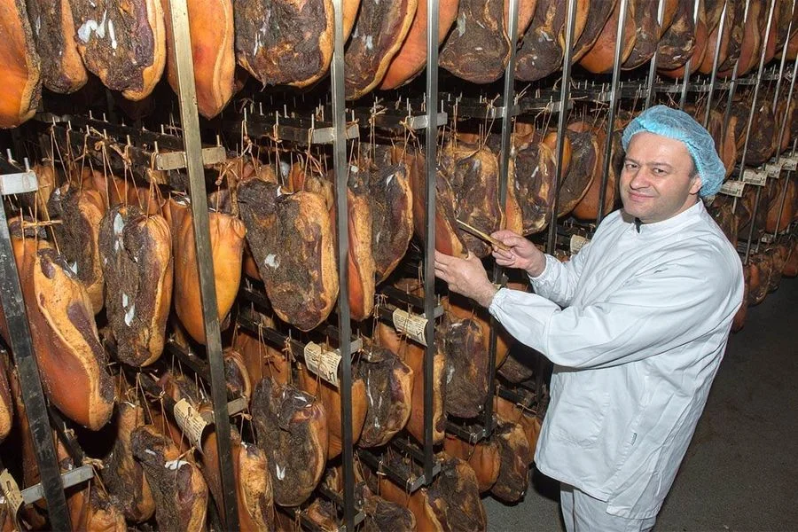 Produttore della Nocker in locale di stagionatura controlla pezzi di Speck Alto Adige IGP appesi