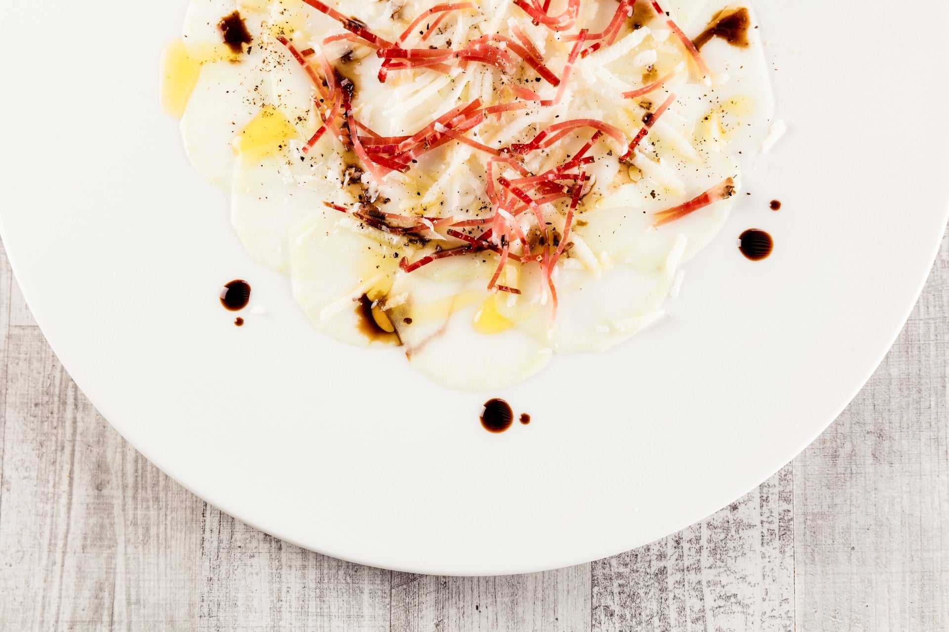 Kohlrabi-Carpaccio mit feinen Scheiben Südtiroler Speck, Parmesan und einem Hauch Balsamico.