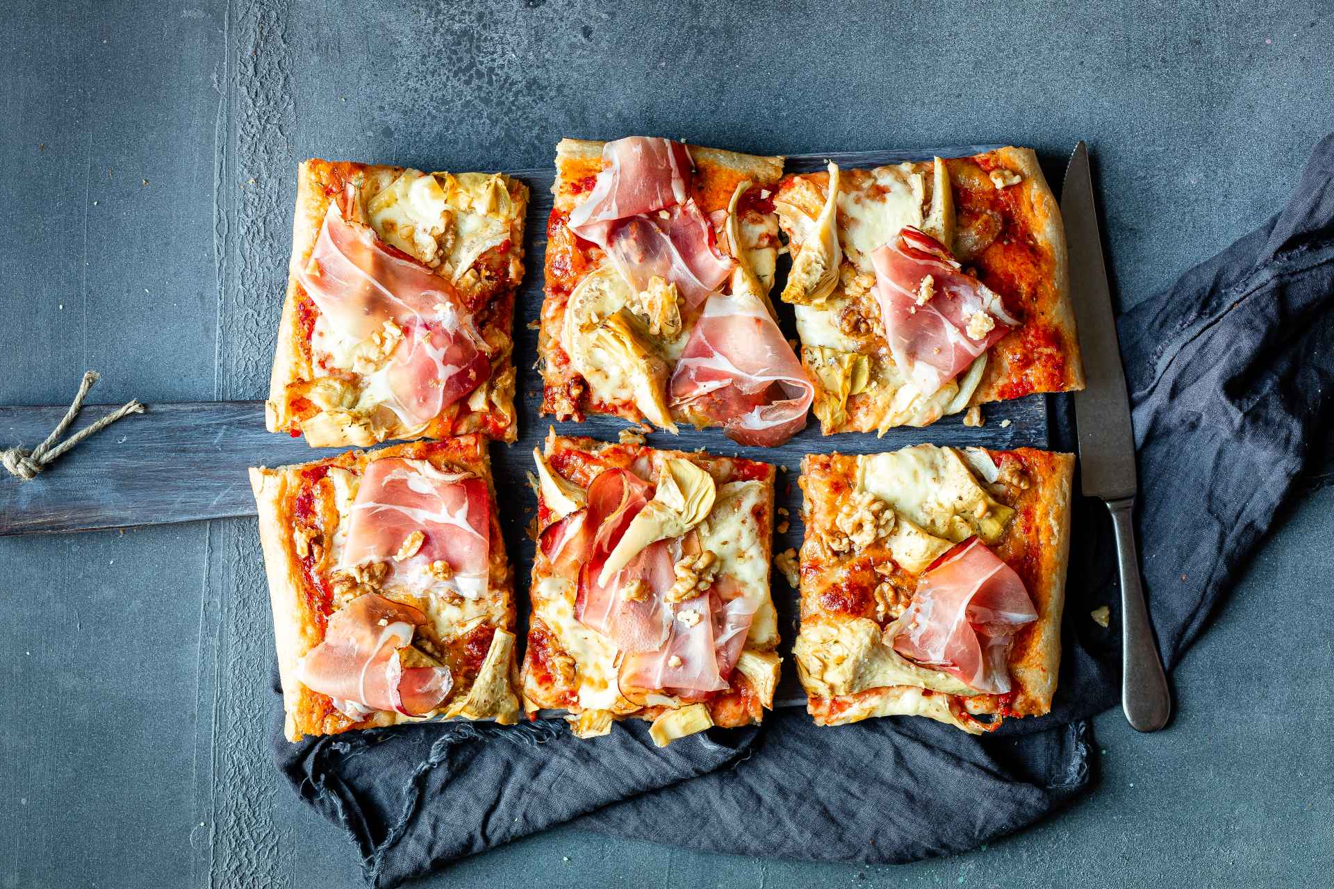 Pizzastücke mit Südtiroler Speck g.g.A., Brie, Artischocken und Walnüssen.