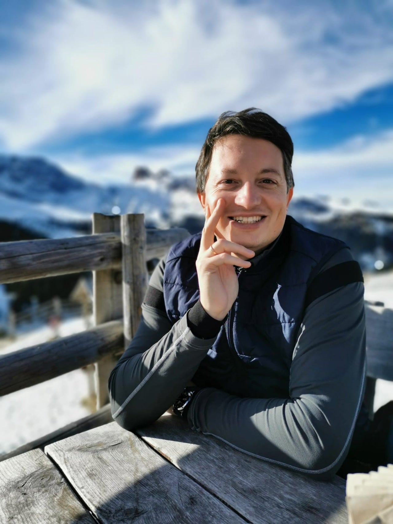 Mitarbeiter des Südtiroler Speck Konsortiums sitzt an einem Holztisch vor winterlicher Südtiroler Bergkulisse.