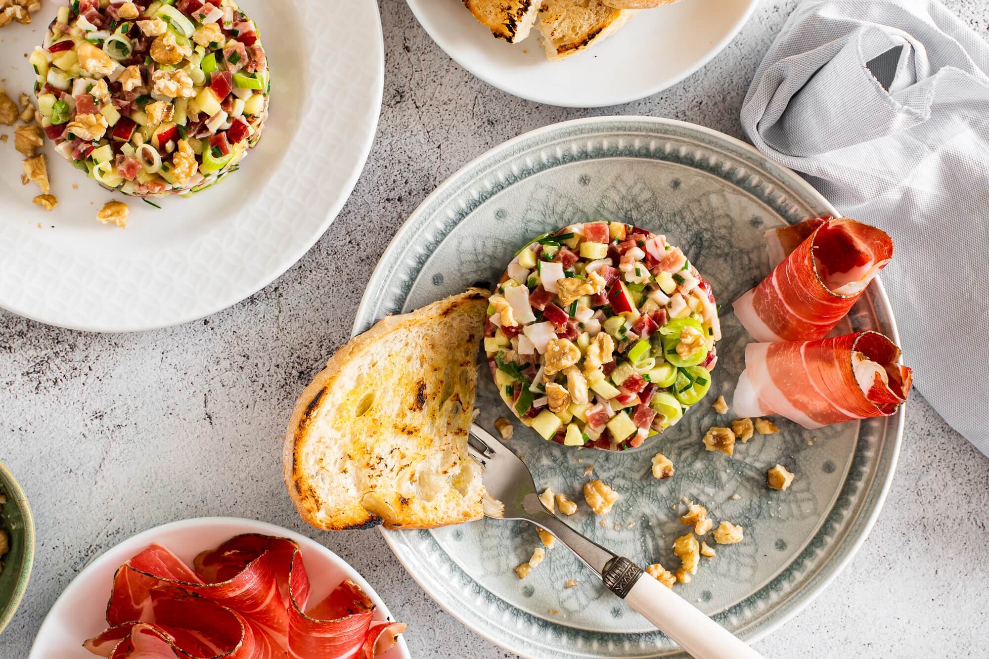 Tatar mit Südtiroler Speck g.g.A., Gemüse und Nüssen auf Teller angerichtet, dazu Brot