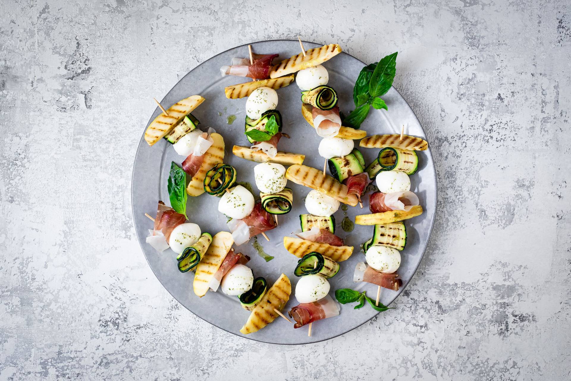 Sommerspieße aus Südtiroler Speck g.g.A., gegrillten Apfelscheiben, gerollten Zucchini und Mozzarella-Bällchen.