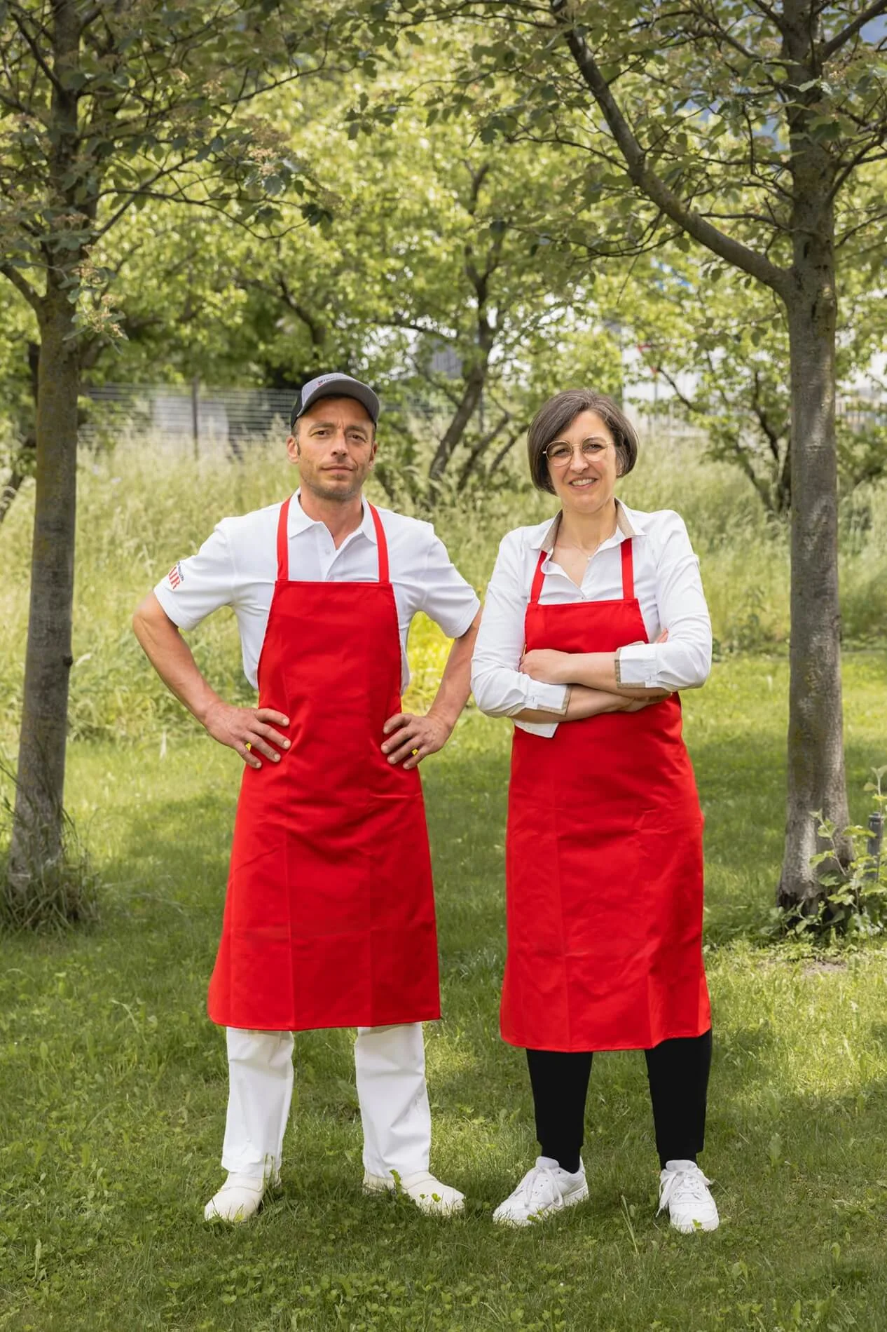 Produttori della Mair con grembiuli rossi in posa all’aperto tra alberi su un prato