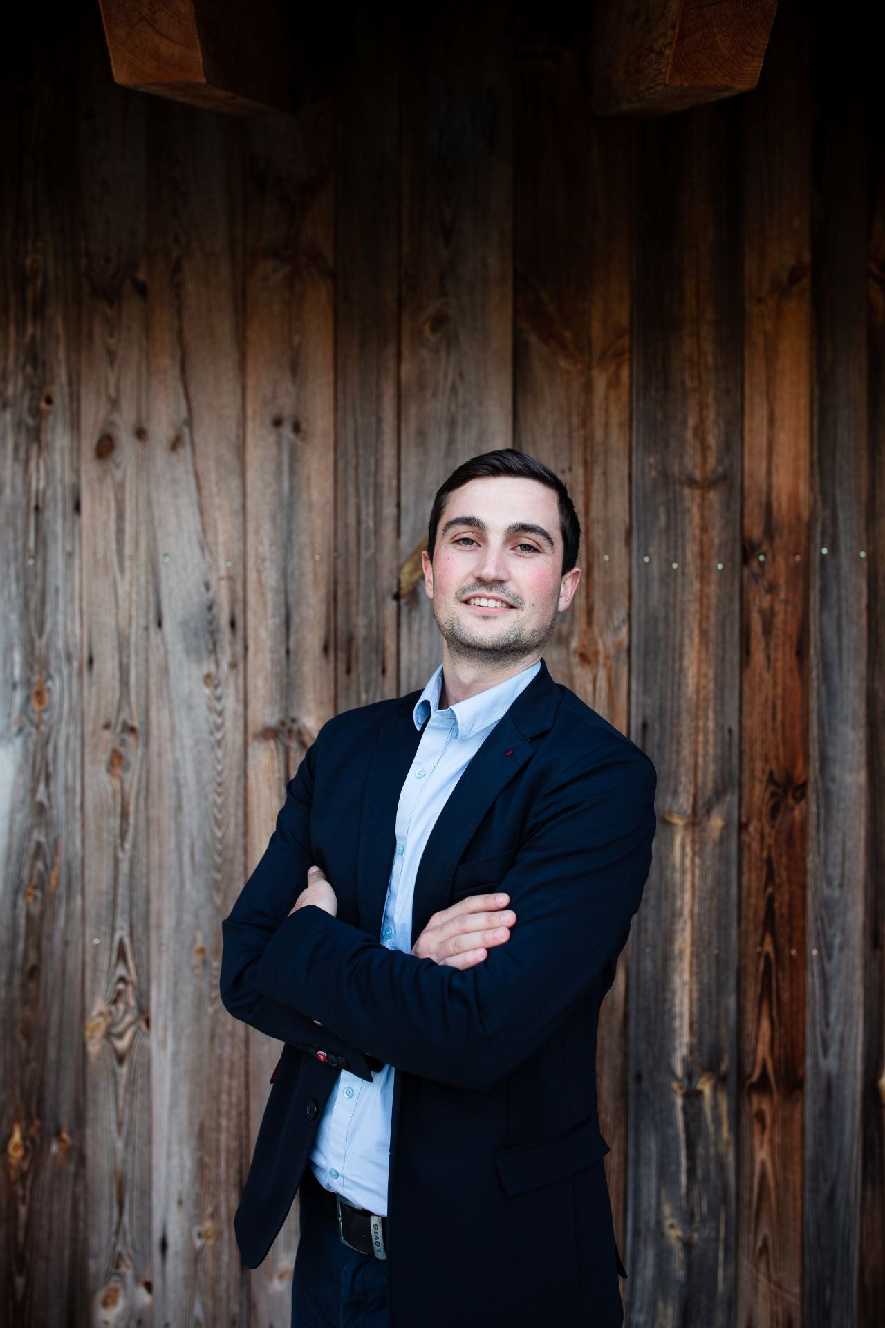 Martin Knoll steht in Pose vor Holzwand mit verschränkten Armen