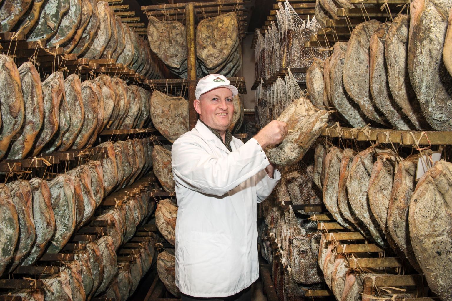 Günther Windegger hält ein Stück Speck Alto Adige g.g.A. im Reiferaum mit hängenden Speckseiten