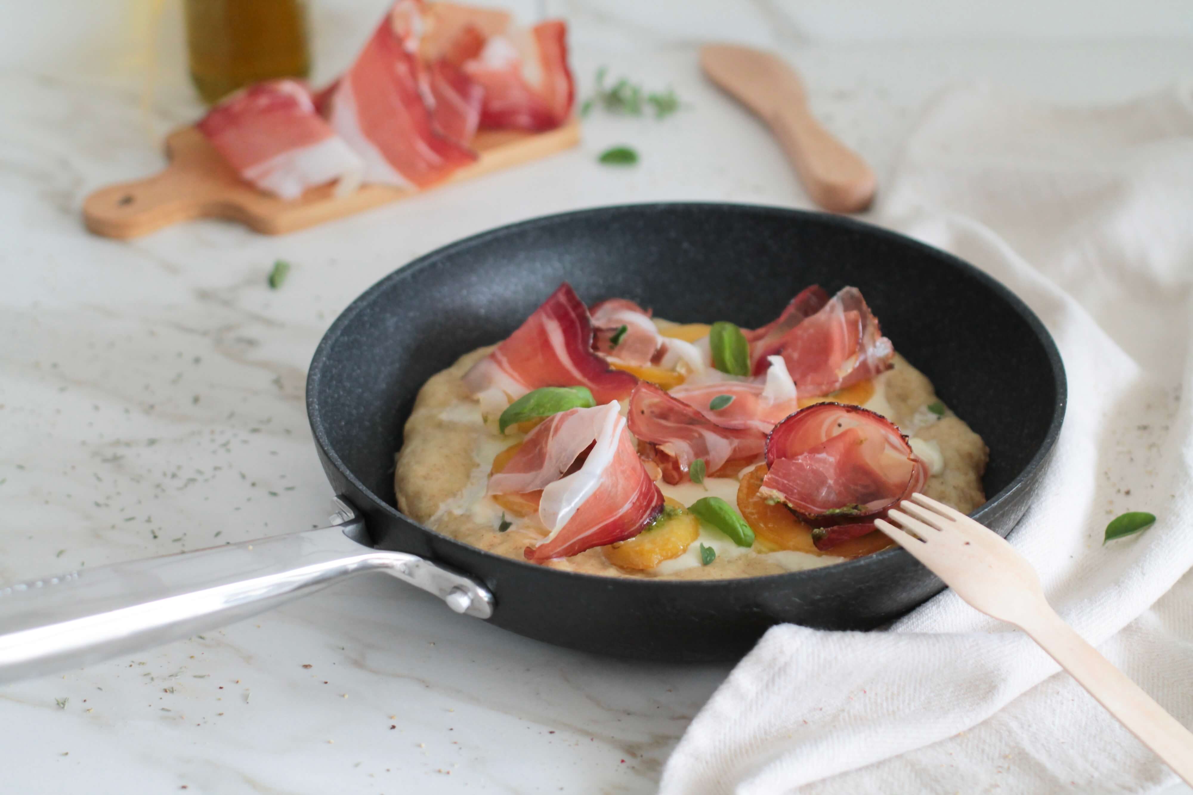 Pizza-in-the-pan with Speck Alto Adige PGI, tomato sauce, mozzarella, boiled potatoes, and pesto.