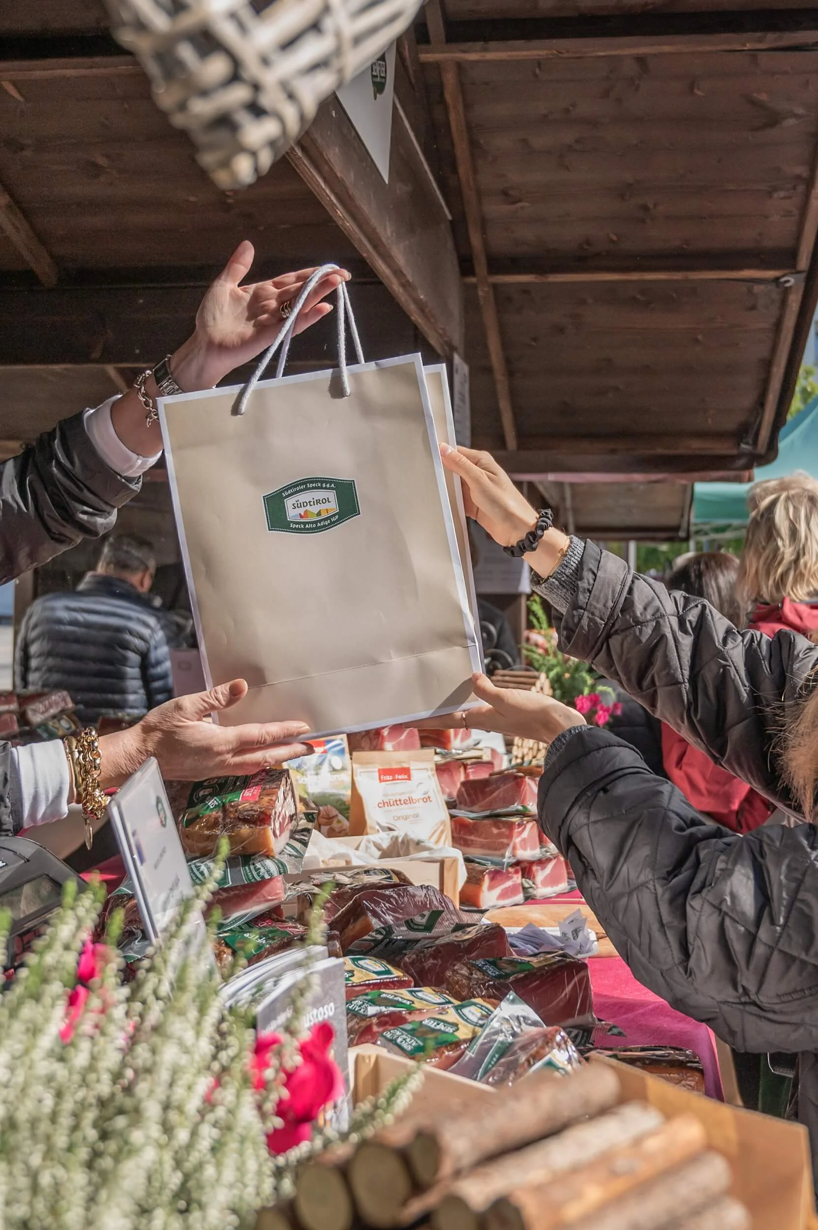 Übergabe einer Tasche mit Südtiroler Speck g.g.A. Siegel an eine Person am Holzverkaufsstand