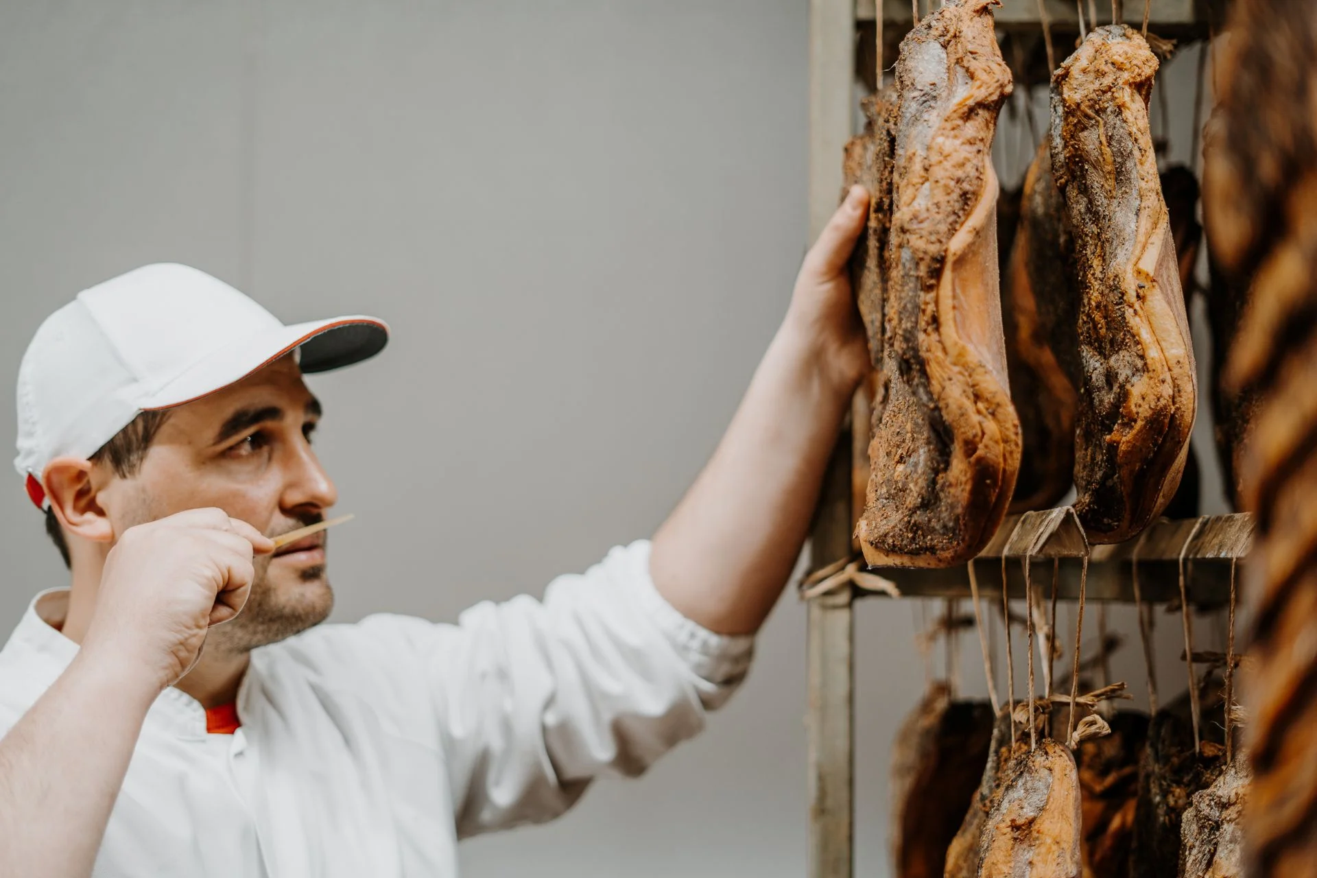 Mann im Kittel prüft ein Stück Südtiroler Speck g.g.A. im Reiferaum