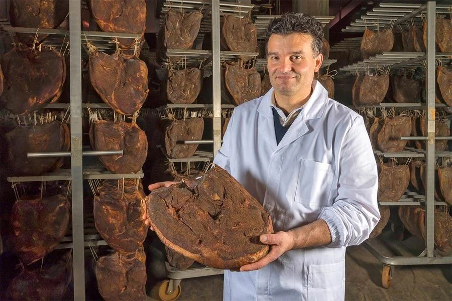 Il produttore Robert Priller regge un pezzo intero di Speck Alto Adige IGP in locale di stagionatura