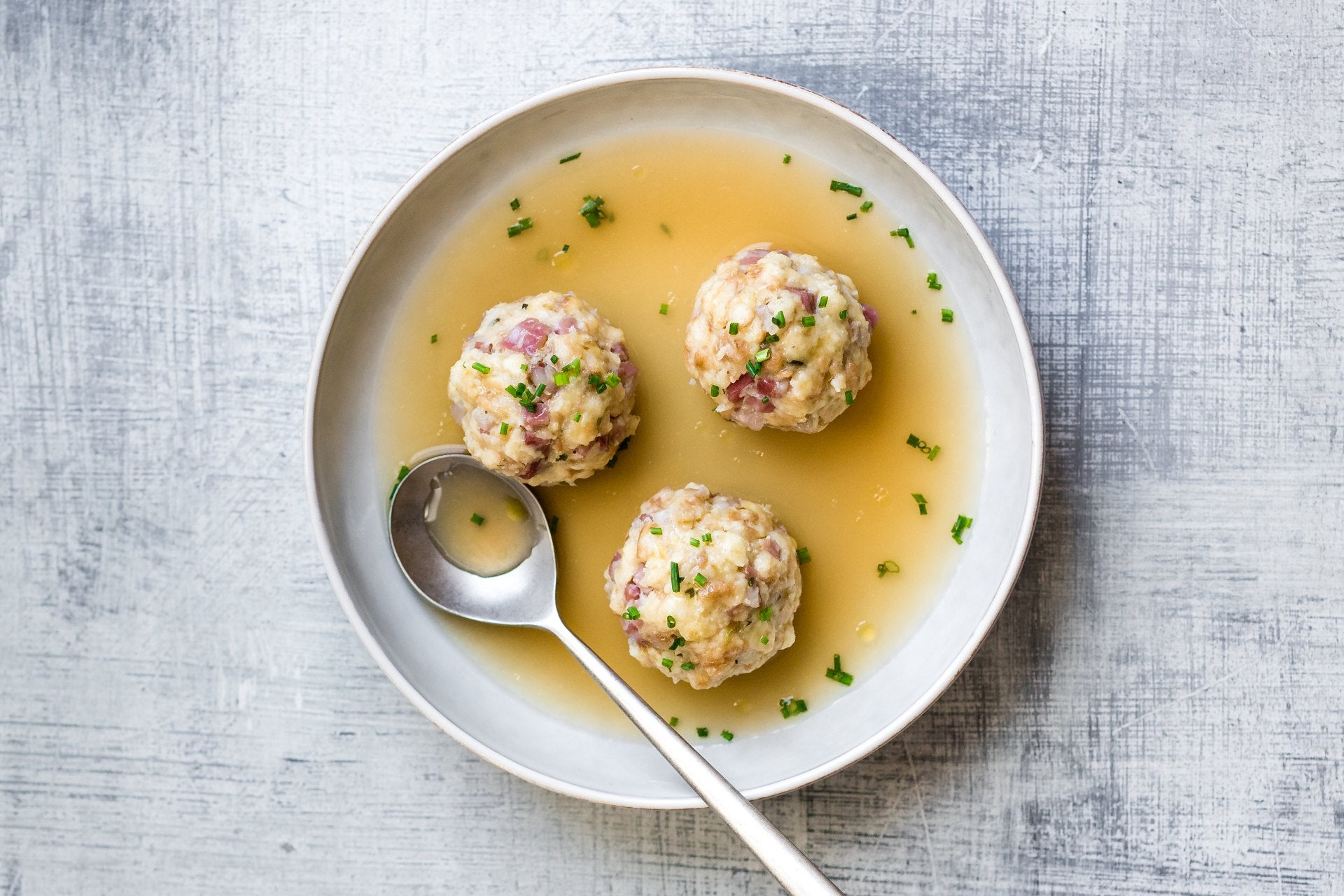 Südtiroler Speckknödel in klarer Brühe mit Schnittlauch, serviert in einem tiefen Teller.