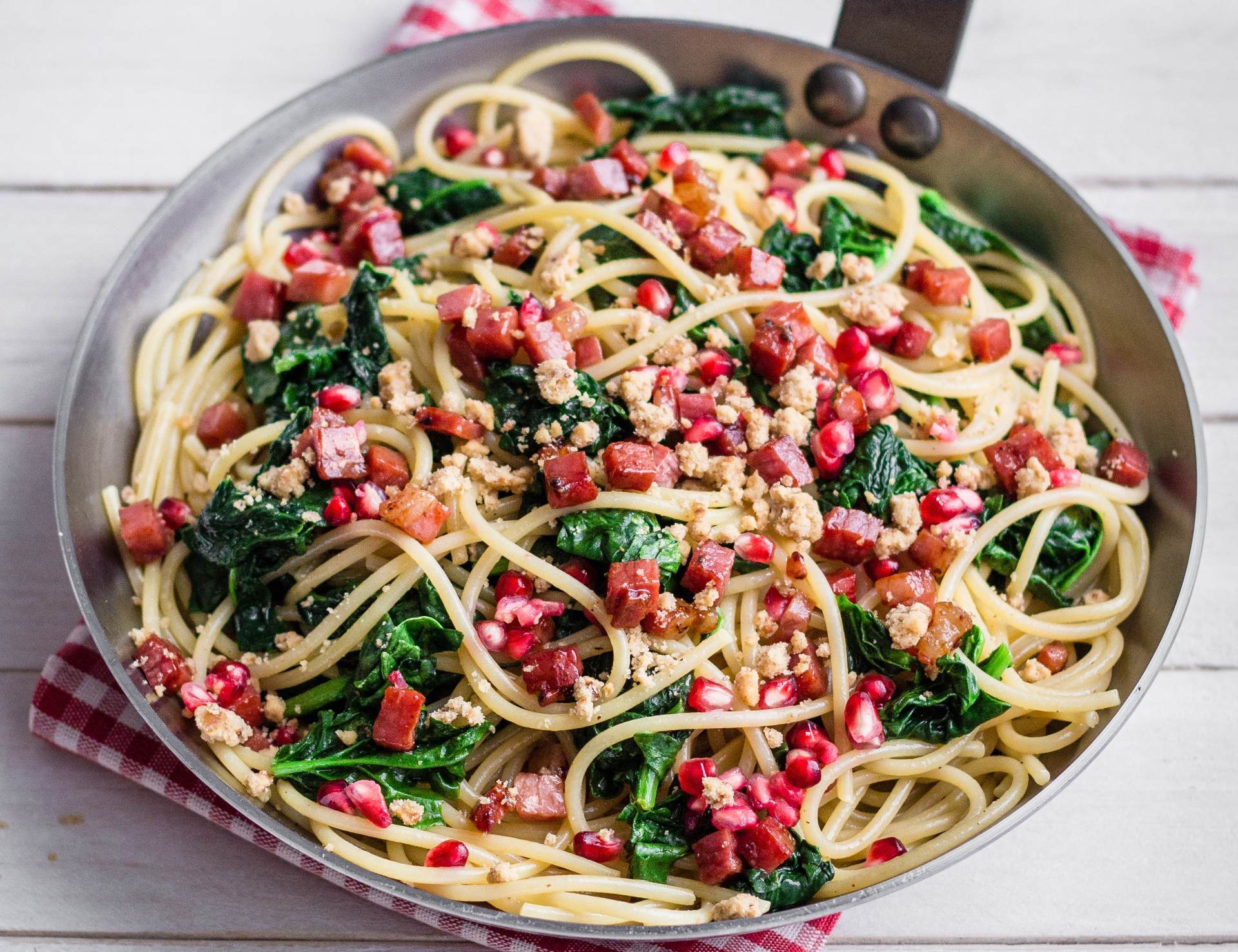 Spaghettoni aux épinards sautés, cubes croustillants de Speck Alto Adige IGP et grains de grenade.