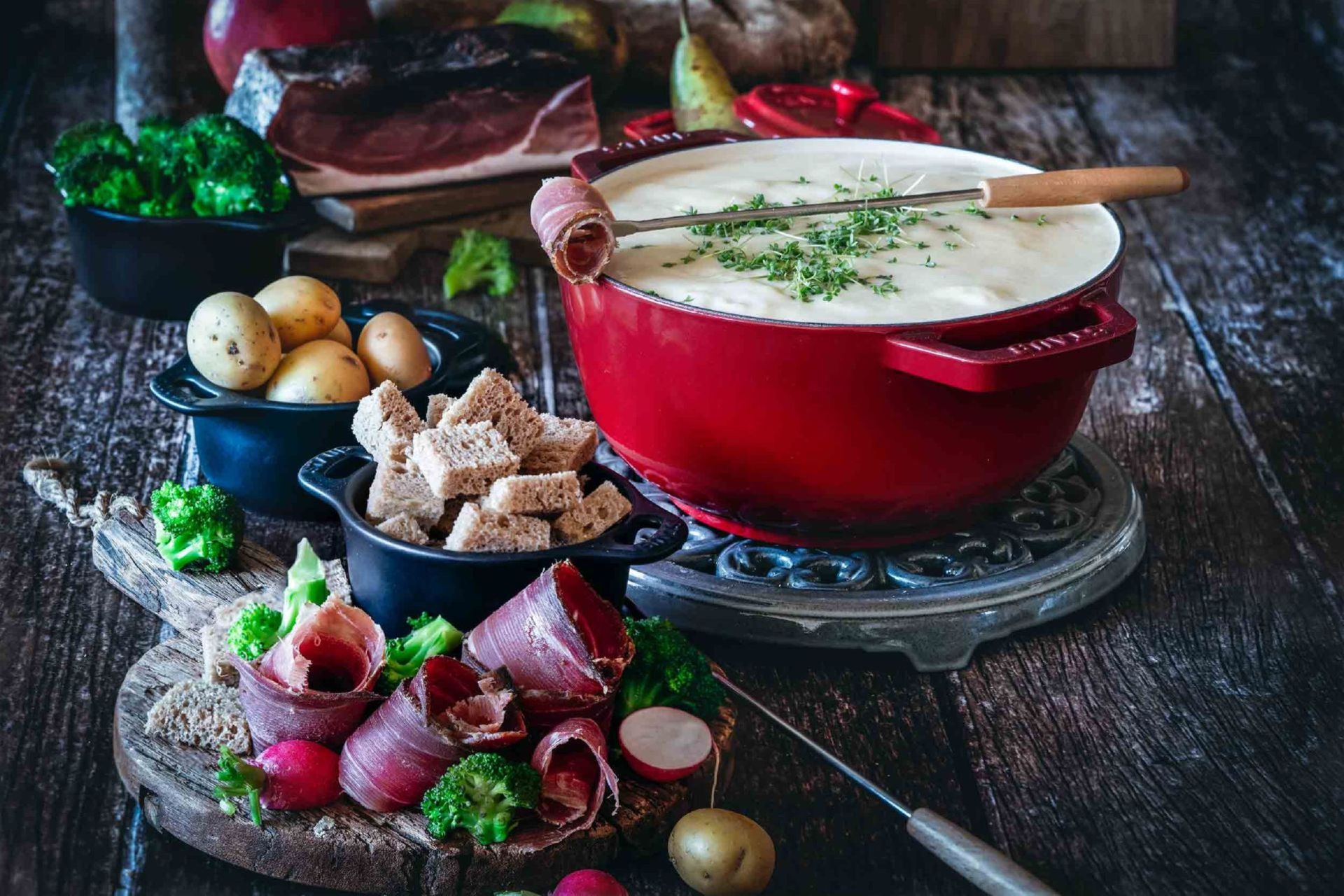 Fondue au fromage en casserole avec Speck Alto Adige IGP, pain, pommes de terre et légumes sur table en bois