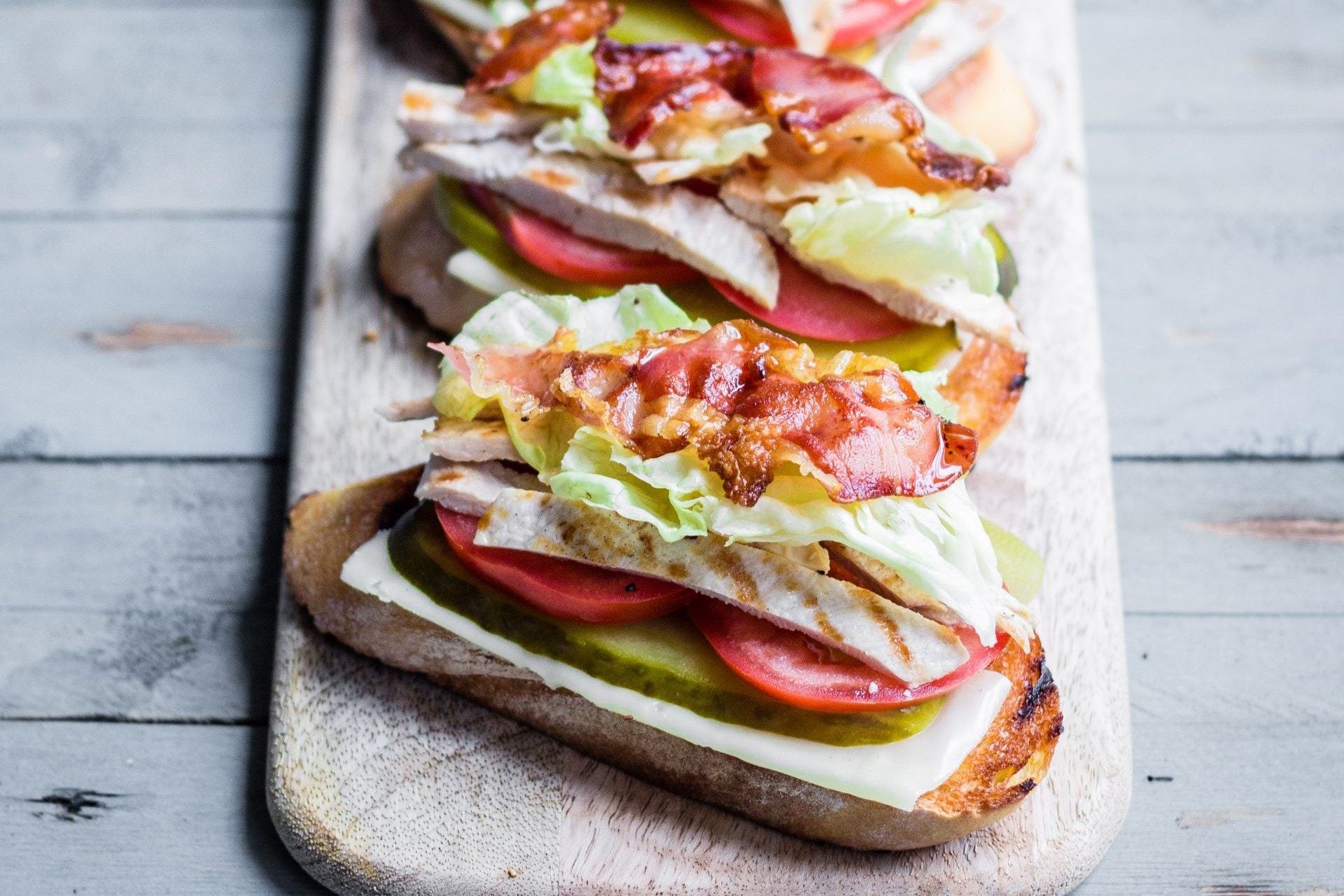 Sandwich garni de speck du Tyrol du Sud IGP, de dinde rôtie, de salade verte et de tomates, servi sur du pain grillé.