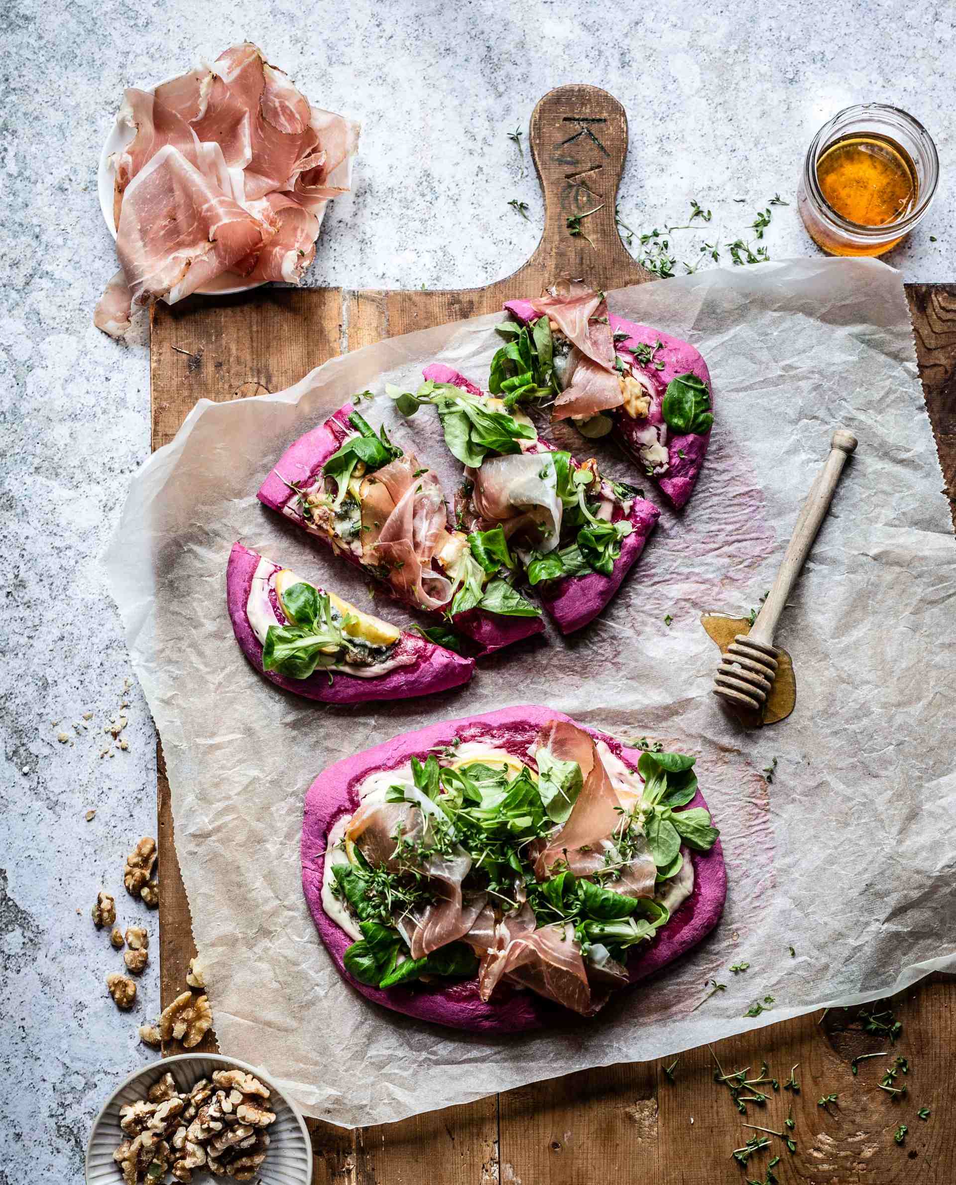 Rote-Bete-Pizza in Stücken geschnitten, mit Südtiroler Speck g.g.A., Blauschimmelkäse, Apfelscheiben, Honig und Walnüssen.