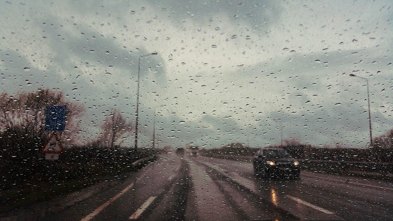Rain drops splattered on a windscreen obscure the view of the wet road ahead