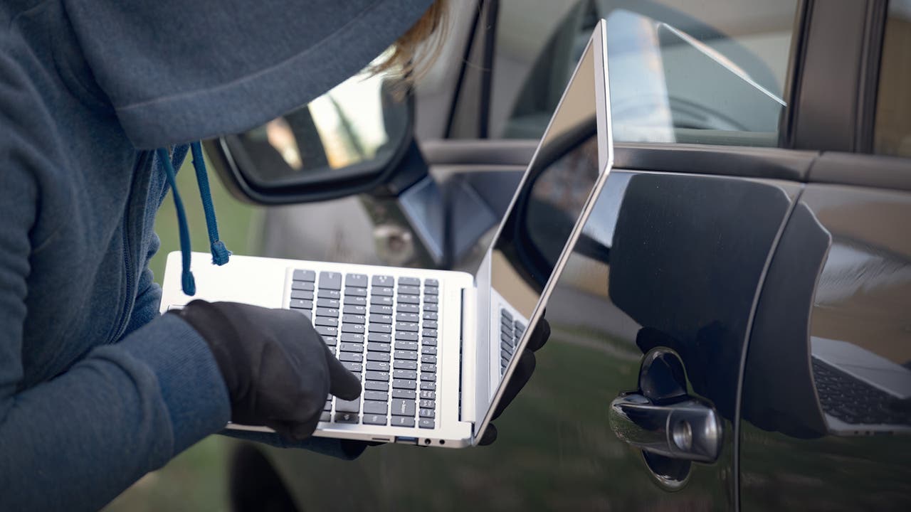 Car thief typing on a laptop next to a car door, which is definitely how most car thefts look