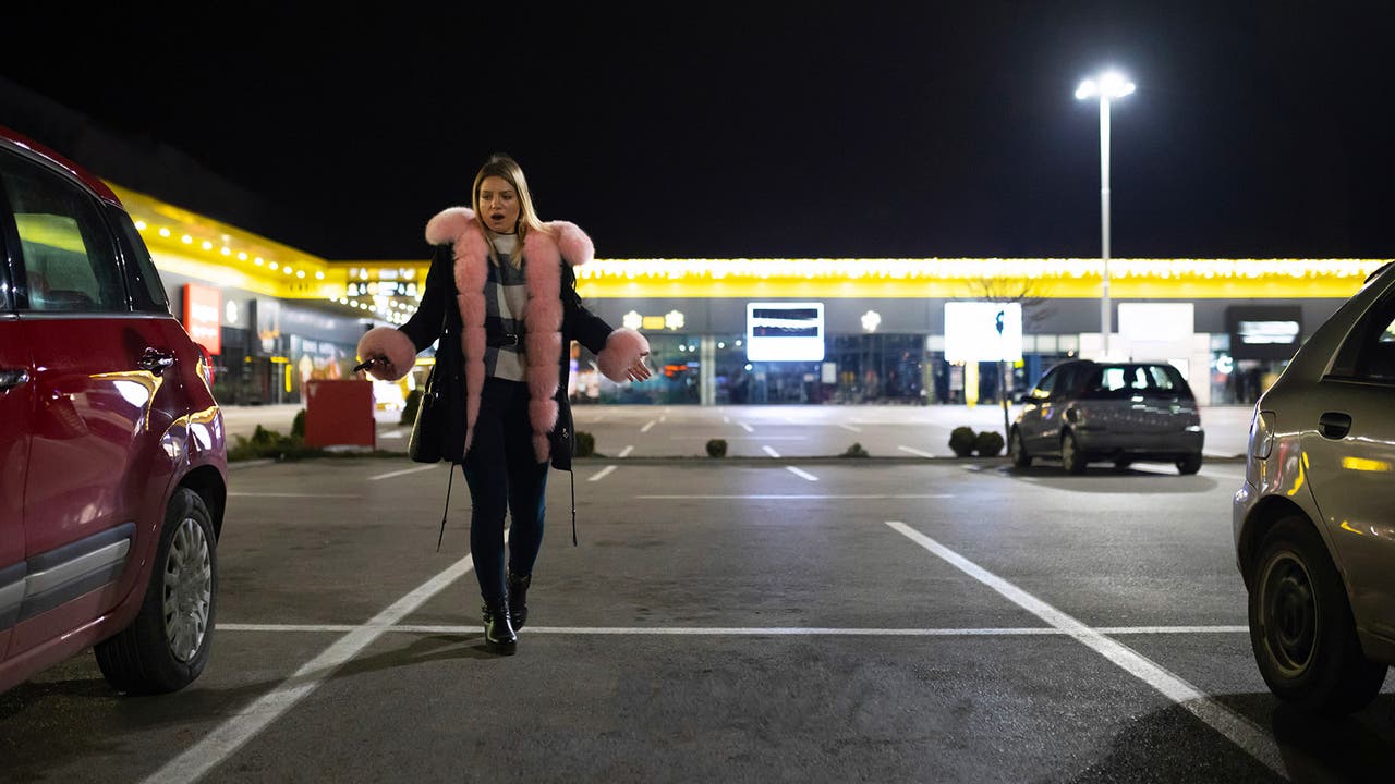 Lady in coat with pink trim expresses her shock at finding her car has been taken from its parking spot