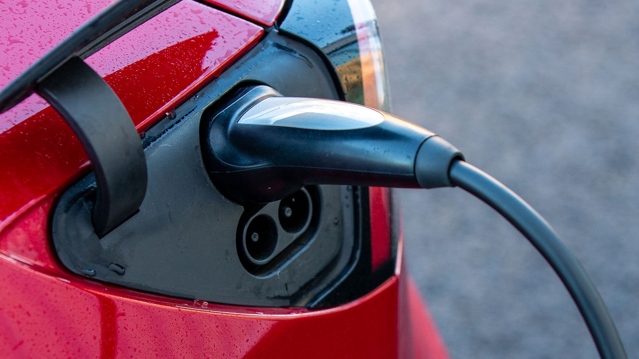 A charger plugged into a red Tesla Model 3's charging port