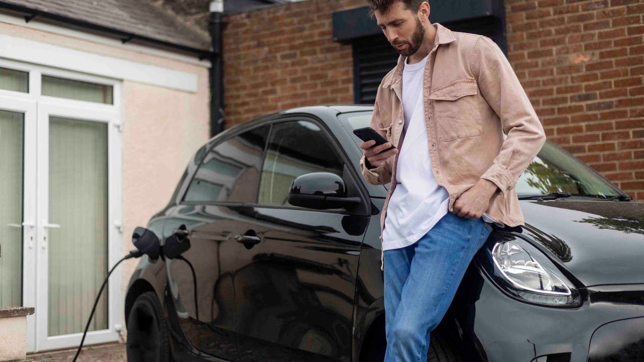 Man looking at phone while charging electric car