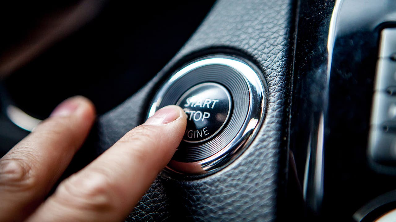 Driver's fingers hover over the stop-start button in a car