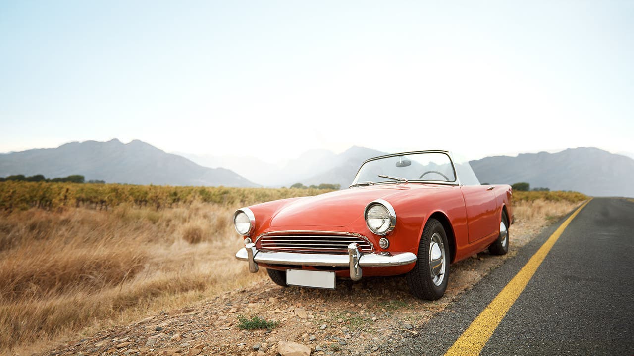 An old red convertible parked by the side of the road