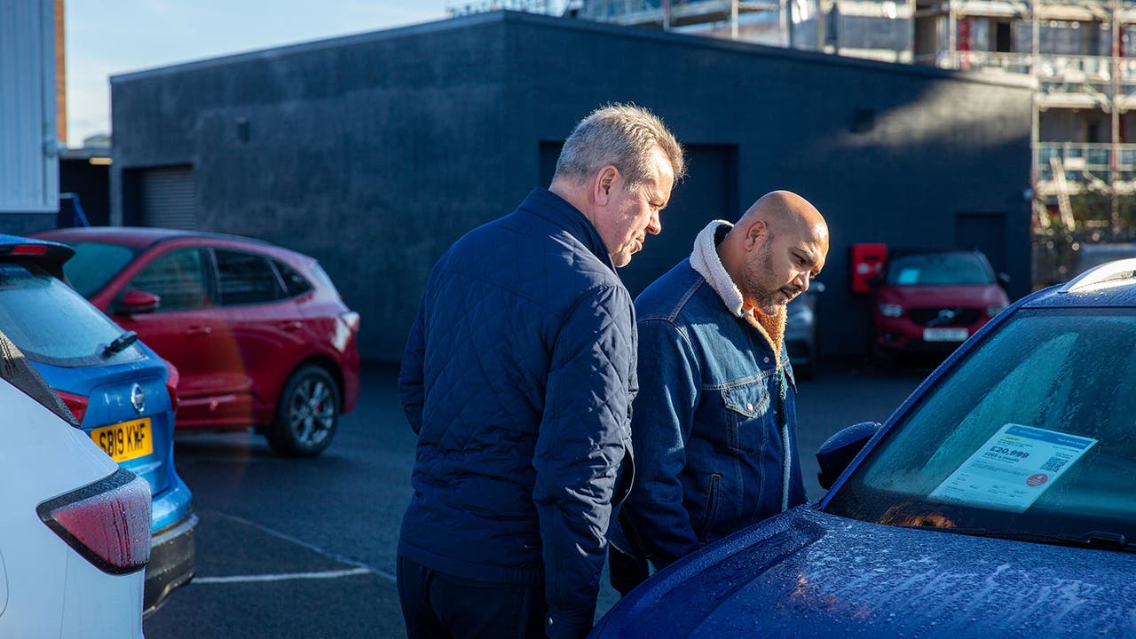 Two car buyers lean over the price tag of a car parked at a Motorpoint store