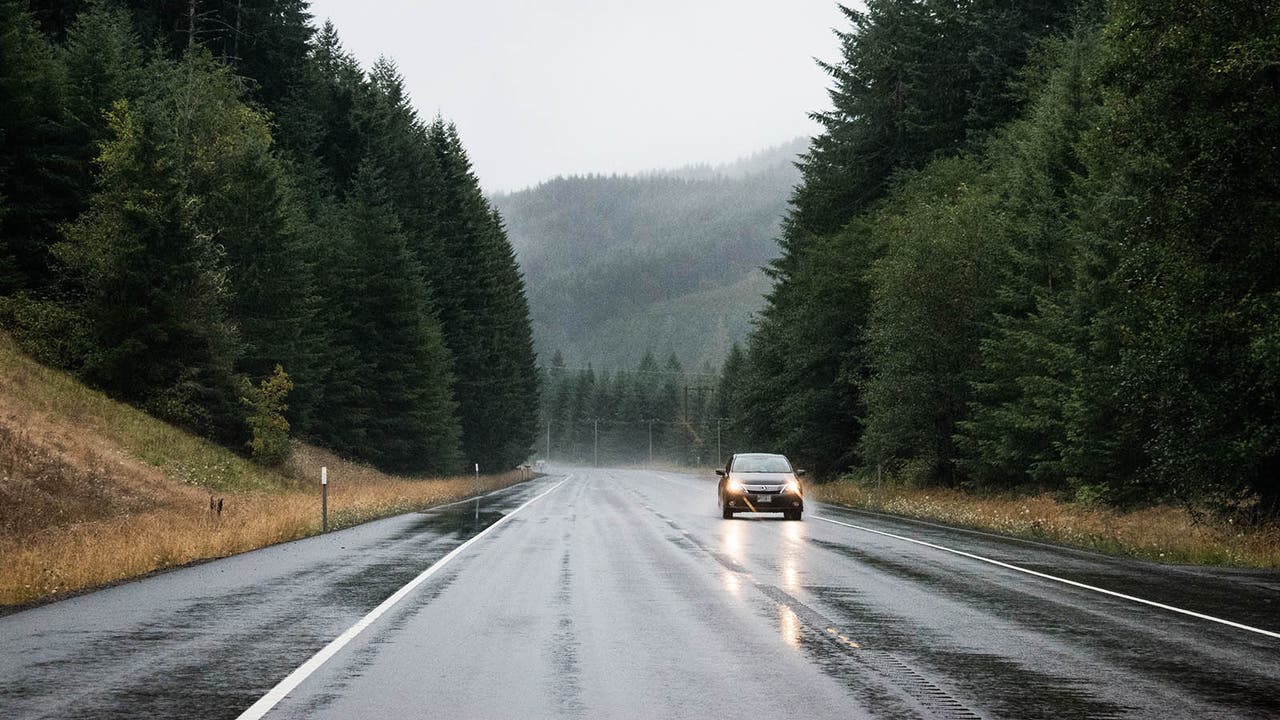 A straight wet road with a single car in the oncoming lane