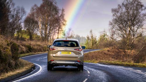 Mazda CX-5 driving rear view, under rainbow