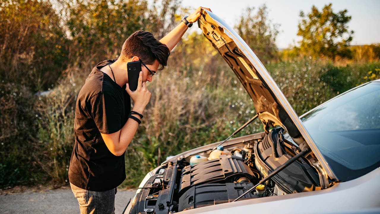 Man looks concerned while checking under his car's bonnet while on the phone