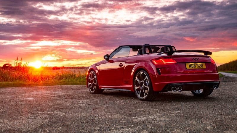 Audi TT (TTS) Roadster in red, rear three quarter in front of a dramatic sunset