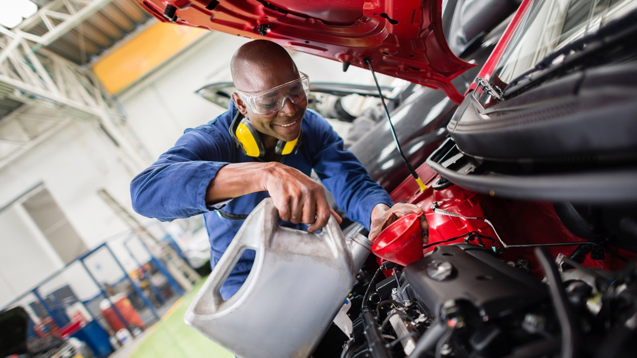 Happy mechanic pours fluid into an engine bay